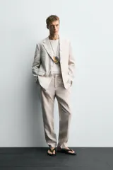 Pantalón de traje regular fit confeccionado en tejido de lino, con bolsillos laterales y bolsillos traseros de vivo con botón. Presenta cierre frontal con cremallera y botón.