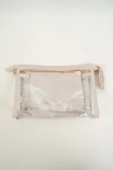 Neceser transparente con bordes y cierre en color beige claro, que incluye un neceser interior más pequeño de color plateado brillante.