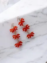 Caravanas colgantes con diseño de flores compuestas por pétalos de acrílico rojo y perlas centrales, unidas por una cadena dorada.
