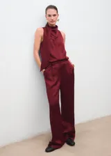 Pantalón wide leg de tiro medio en tejido satinado color bordó, con pinzas delanteras, trabillas, bolsillos laterales y cierre oculto con botón, gancho y cremallera.