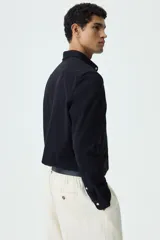 Camisa negra de punto elástico con cuello italiano, cierre frontal de botones y mangas largas.