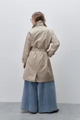 Trench clásico color marrón, de silueta relajada, confeccionado en tejido liviano, con cuello de solapa, doble abotonadura frontal y mangas largas con presillas regulables en los puños.