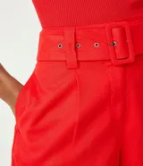 Short rojo de lino con cintura alta, cinturón con hebilla cuadrada forrada, pliegues delanteros y dos bolsillos laterales.