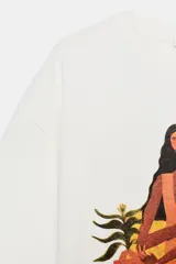 Remera oversize de algodón color crudo con cuello redondo y manga corta. Presenta una ilustración artística estampada y bordada en el frente que representa a un grupo de mujeres.