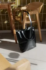 Cartera tipo tote bag de cuero marrón, con diseño minimalista, asas largas y detalles de remaches metálicos en la unión de las asas.