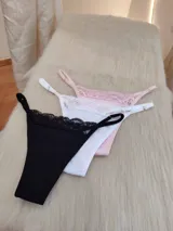 Pack de tres tangas de algodón en colores rosa, blanco y negro, con detalle de encaje en la parte superior y tiras regulables.