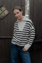Buzo de punto con diseño a rayas horizontales en blanco y negro. Presenta cuello alto con cierre frontal parcial y mangas largas con puños acanalados.