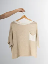 Remera tejida color crema con cuello redondo y bolsillo frontal verde.