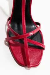 Sandalias rojas de taco fino y alto, con diseño de tiras finas en el empeine, tira en T y pulsera ajustable con hebilla en el tobillo.