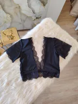 Top de encaje y lycra color negro, con escote profundo en V adornado con puntilla, mangas cortas de encaje y diseño con transparencias de microtul en los laterales y espalda.