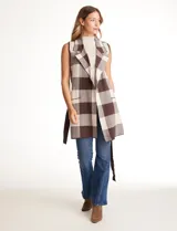 Chaleco tejido largo de la marca Absolutely Famous, con estampado a cuadros en tonos marrón, beige y blanco. Presenta cuello con solapa, abertura central, bolsillos aplicados en la parte delantera, pasadores en la cintura con lazo de ajuste y un tajo central en el ruedo trasero.