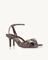Sandalias de cuero color borgoña con taco fino y pulsera al tobillo. Presentan un aplique metálico dorado en forma de cuadrado en la parte delantera.