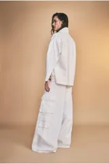 Chaqueta color blanco hueso, de corte recto, con cuello camisero, cierre frontal con botones y bolsillos de parche en el pecho.