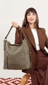 Cartera de hombro tipo hobo en color negro, confeccionada en material símil cuero con textura granulada. Presenta un diseño funcional con cierre principal, bolsillo frontal con cierre y detalles de tachas metálicas, además de una correa de hombro fija y una correa larga ajustable y extraíble.