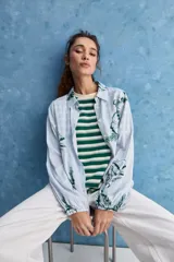 Camisa de calce relajado con cuello clásico, mangas largas con puños elastizados y rayas verticales que aportan un estilo atemporal. Su diseño liviano y versátil cuenta con estampado floral verde sobre fondo de rayas celestes y blancas.