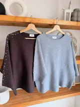 Sweater gris melange con detalles de perlas y strass aplicados en las mangas, de corte holgado y mangas largas.