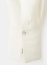 Blusa de modal y poliéster color blanco marfil, con diseño recto, escote en V, mangas largas y detalle de fular incorporado en el cuello. Cierre frontal con botones.