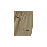 Pantalón de jogging Fear of God Essentials de corte acampanado, color beige, con cintura elástica con cordón ajustable, parche de goma con el logo de la marca y texto "Essentials" bordado en la pierna.