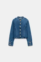 Chaqueta de denim azul con cuello redondo, manga larga y cierre frontal con botones dorados. Presenta costuras verticales decorativas y puños con botones a juego.
