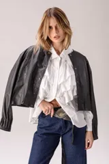 Camisa blanca de corte clásico con volados frontales y en los hombros, manga larga con puños abotonados y cierre frontal con botones.