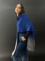 Ruana azul con degradé a gris, confeccionada en lana merino fina y suave, teñida artesanalmente. Presenta cuello plisado en fieltro de lana merino.