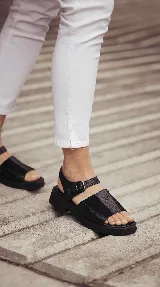 Sandalia de cuero color negro con combinación de texturas, base de goma liviana, diseño chunky, tiras anchas en el empeine y tira con hebilla ajustable en el tobillo.