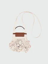 Bolso de mano tipo cesta de la línea Le Pliage Mesh de Longchamp, en tamaño XS. Presenta una estructura de red tejida en color marfil con detalles de lazos bordados en tonos pastel y asas cortas de cuero marrón. Incluye una correa larga ajustable para llevar al hombro o cruzado.