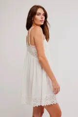 Vestido corto tipo slip dress color blanco, de corte amplio tipo babydoll, confeccionado en mezcla de viscosa y algodón. Presenta escote en V con apliques de encaje, tiras finas regulables y ruedo festoneado con detalles de encaje y calados.