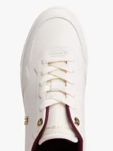 Zapatillas de cuero estilo tenis, color blanco, con cordones y suela de goma al tono. Presentan forro interior en color bordó, ojal superior metálico dorado y logo de monograma TH metálico en el lateral.