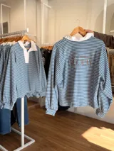 Buzo tipo chomba de corte oversize con diseño a rayas horizontales celestes y blancas. Presenta cuello camisero blanco y un bordado en la espalda con la inscripción República Oriental del Uruguay.
