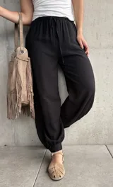 Pantalón negro tipo babucha con cintura elástica fruncida y cordón ajustable, corte holgado y puños elásticos en los tobillos.