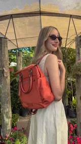 Cartera mochila de diseño versátil en color terracota, confeccionada en material sintético impermeable. Cuenta con doble asa de mano, correas ajustables para usar como mochila, compartimento principal con cierre y bolsillos laterales.