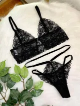 Conjunto de lencería compuesto por un bralette de encaje negro con cierre frontal de gancho y breteles regulables, y una tanga de encaje con tiras elásticas laterales ajustables y argollas metálicas.