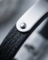 Pulsera de diseño minimalista compuesta por una banda de cuerina negra y una placa central de acero inoxidable con remaches decorativos.