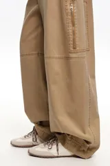 Zapatillas deportivas de color beige y crudo, confeccionadas en serraje vacuno con inserciones de tela, cordones marrones y suela de caucho con tacos. Cuenta con detalle de piel marrón en la parte trasera con logo.