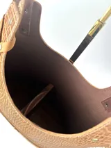 Bolso matero de cuero color marrón con textura tipo piel de cocodrilo en la parte superior y cuero liso en la parte inferior. Tiene dos asas de hombro, cierre superior y detalle de flecos de cuero en un lateral.