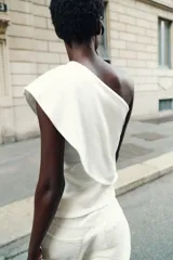 Top blanco de tejido de punto elástico, con escote asimétrico y una manga corta.