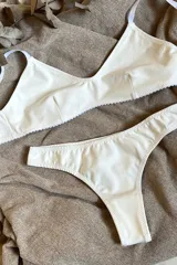 Conjunto de lencería compuesto por un soutien triangular de algodón con breteles regulables y una bombacha tipo tanga a juego, ambos en color blanco.