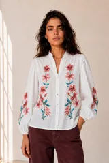 Camisa blanca de manga larga con bordados florales en tono rojo y verde en el frente y las mangas. Presenta cuello mao con escote en V y botones frontales.
