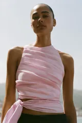 Top halter entallado de popelina color rosado, con diseño de pliegues en diagonal y lazo ajustable en el bajo. Cuenta con cierre lateral con cremallera oculta en la costura.