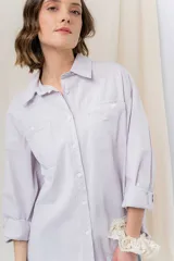 Camisa verde pastel de algodón, corte oversize, con cuello camisero, cierre con botones, mangas largas con puños con volados de encaje blanco, dos bolsillos frontales con solapa y ruedo irregular. 