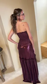 Vestido largo strapless de lamé elastizado color bordó, con cuerpo fruncido tipo corsel y falda larga amplia con volados y frunces.