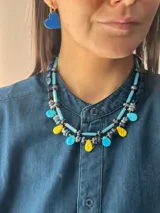 Collar corto de diseño artesanal compuesto por cuentas cilíndricas de vidrio en tono celeste y pequeñas piedras naturales esféricas en tonos azulados, intercaladas con detalles metálicos. Incluye cadena de acero quirúrgico para ajuste de largo.