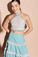 Top halter con acabado brillante, escote alto y detalles de ojalillos decorativos en los bordes. Diseño con espalda descubierta y cierre ajustable.