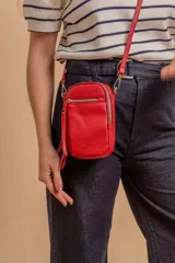 Bandolera porta celular color negro, confeccionada en símil cuero con textura granulada. Presenta un compartimento principal con cierre, un bolsillo frontal con cierre y detalle de borla decorativa, y correa regulable y desmontable.