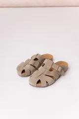 Zuecos de gamuza color beige, con diseño tipo sandalias romanas de tiras anchas entrelazadas, hebilla lateral metálica regulable y suela anatómica de corcho.