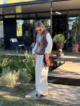 Chaleco tejido de punto en color chocolate, con cuello redondo y diseño sin mangas. Presenta un aplique frontal decorativo compuesto por tres figuras en forma de rombo en tonos tierra, bordeadas con hilo crudo.