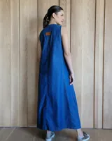 Vestido largo de denim azul, con escote en V, sin mangas, corte holgado, bolsillos laterales y aberturas en los costados de la falda.