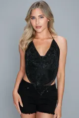 Top negro de malla metálica con brillos, escote halter pronunciado y diseño con terminación en punta en la parte inferior y espalda descubierta.