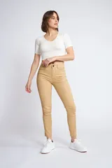 Pantalón de gabardina corte skinny, color beige, con diseño de cinco bolsillos, cierre de cremallera y botón frontal.